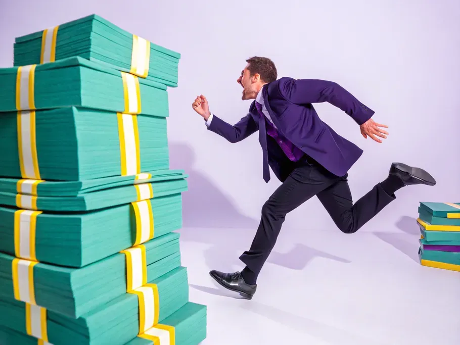 Businessman running towards a large stack of oversized money bundles