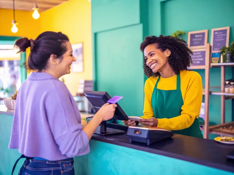 A friendly cashier recording a sale and handing a product to a customer in a cozy shop.