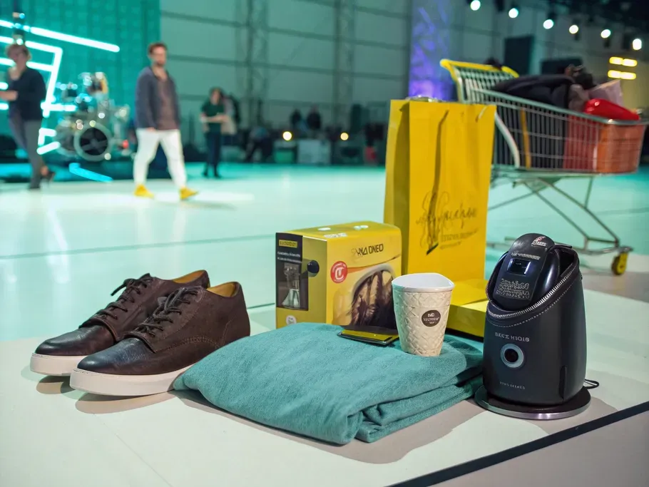 Diverse merchandise items including a stylish shoe, a gadget, a gourmet coffee bag, and a folded textile on a bright stage.
