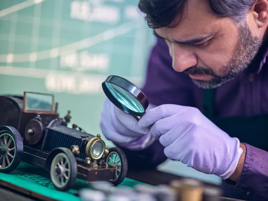 A professional appraiser examining a vintage car model with a magnifying glass, symbolizing the valuation of tangible assets.