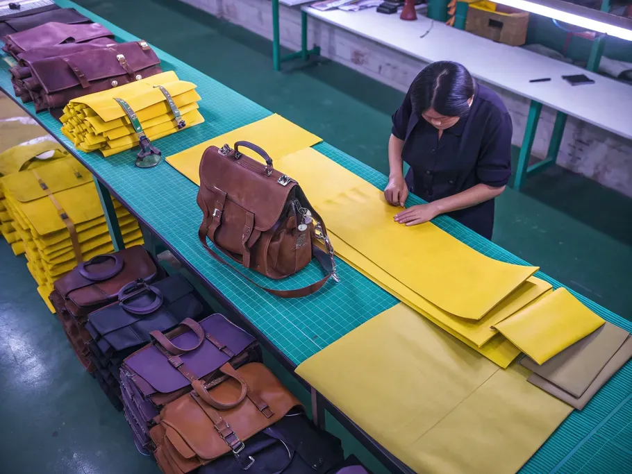 A top-down view of a production line showcasing the transformation of leather hides into finished bags.